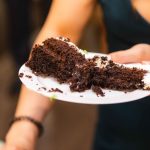 A person holding a piece of chocolate cake at a birthday party.