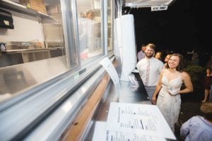 A bride and groom enjoying their wedding reception in front of a food truck.