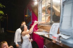 A bride and groom enjoying a food truck at their wedding reception.