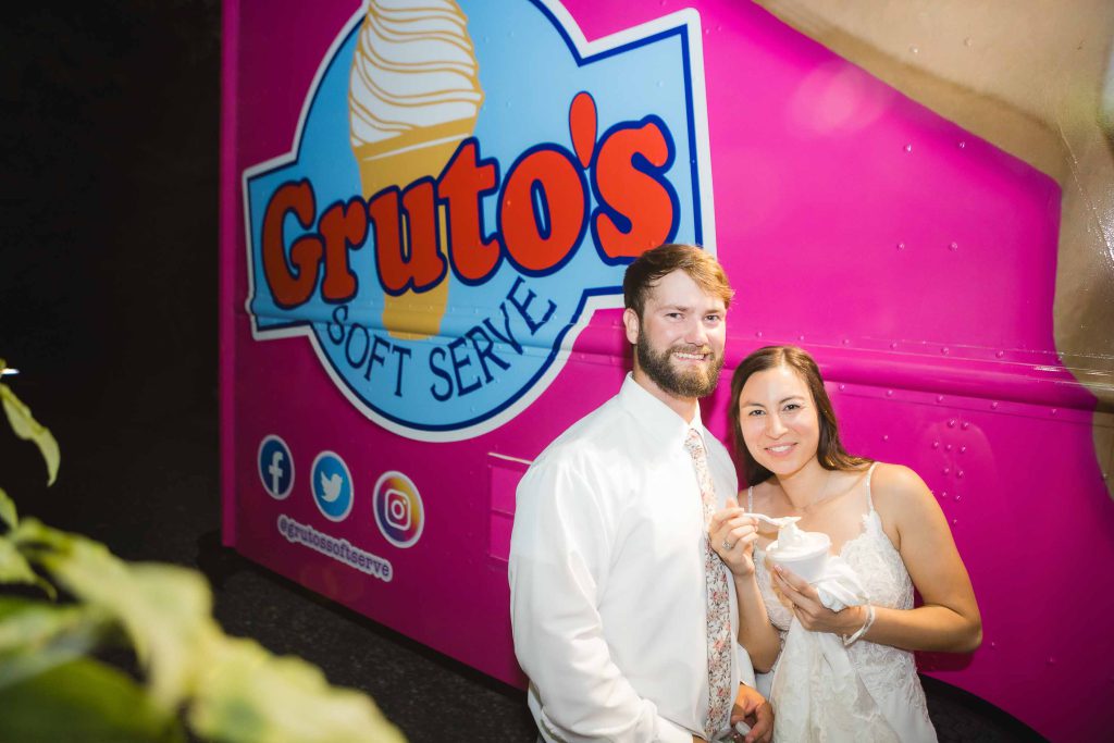 A bride and groom pose in front of a wedding-themed ice cream truck at their reception.