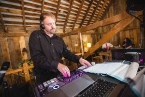 A man playing a DJ at a wedding reception in a barn.