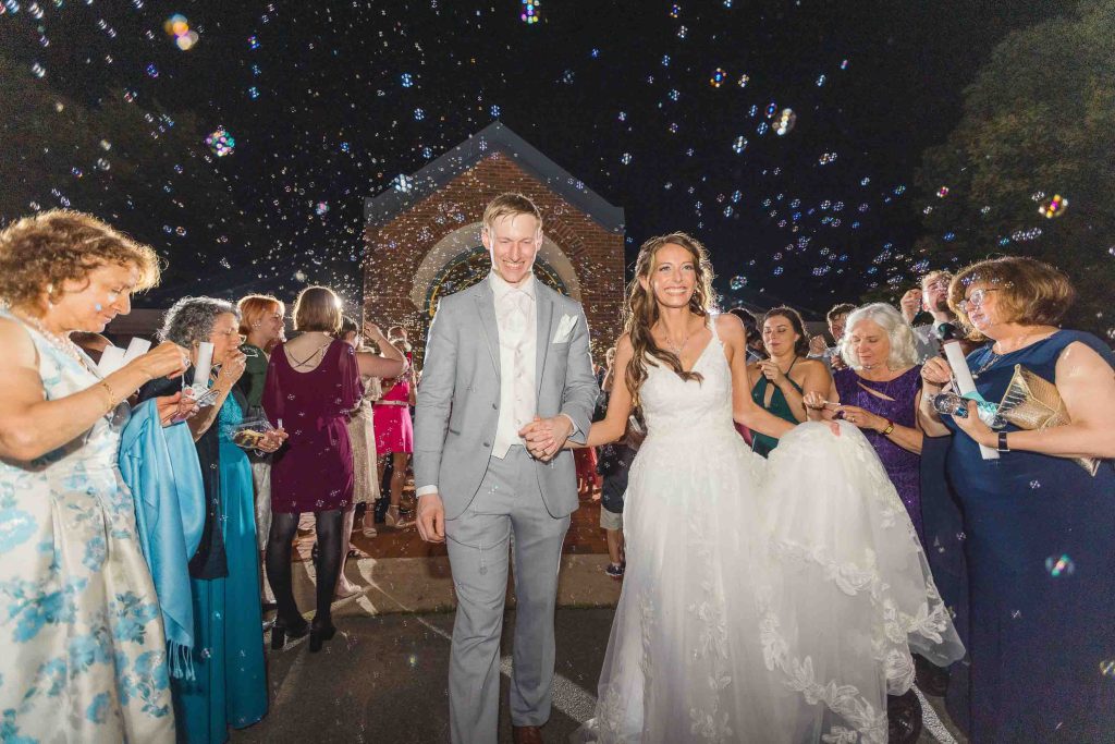 A bride and groom exiting a church after their wedding with bubbles thrown at them during their reception.