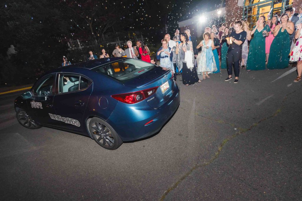 A group of people standing around a car at night during a wedding reception.