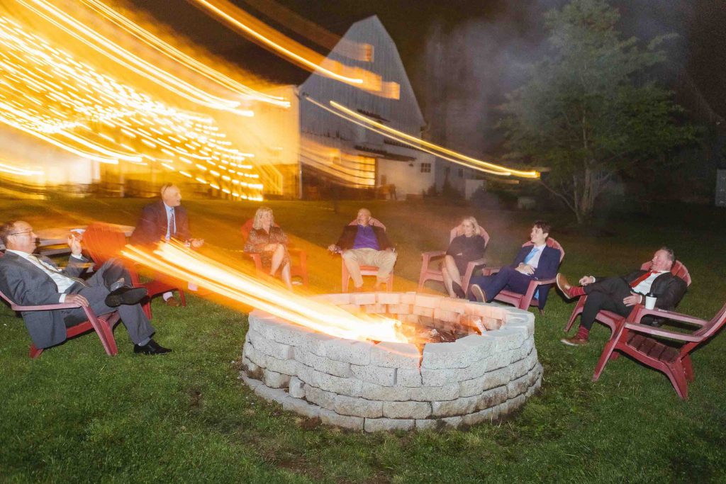 A wedding reception with people sitting around a fire pit at night.