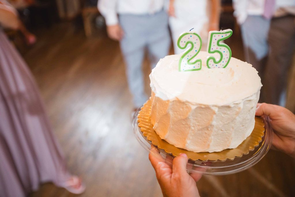 A woman is holding a wedding cake with the number 25 on it.