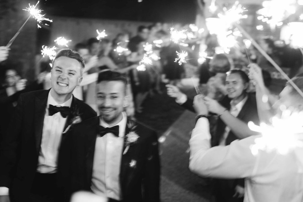 A black and white photo of groomsmen holding sparklers at a wedding reception.