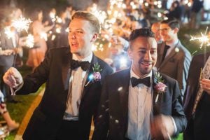 Two men in tuxedos holding sparklers at a wedding reception.
