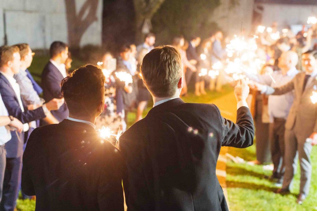 A group of men holding sparklers at a wedding reception.