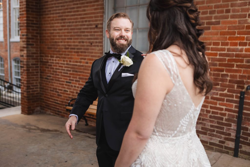 A bride and groom sharing a candid moment at their wedding in front of the historic brick building at Savage Mill.