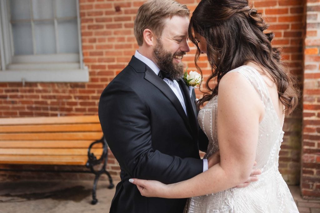 A wedding couple embraces candidly in front of the Savage Mill.