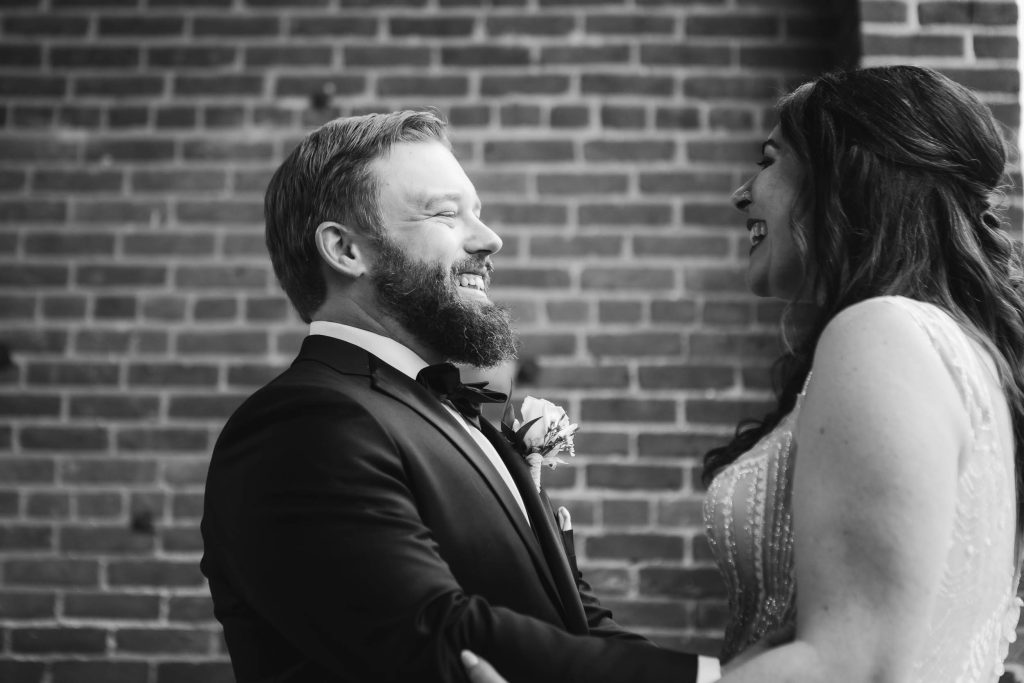 A candid bride and groom share a heartfelt moment in front of a brick wall at their wedding venue, Savage Mill.