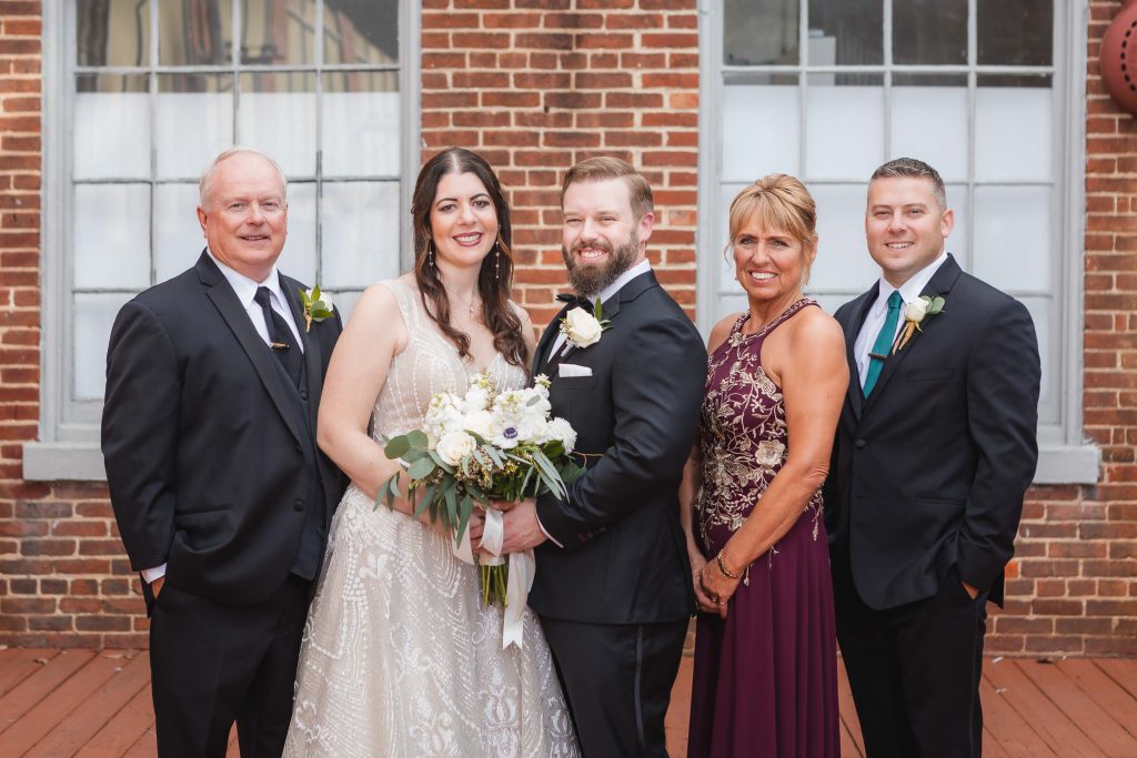 The wedding party, including the bride and groom, poses for portraits in front of The Great Room at Savage Mill.