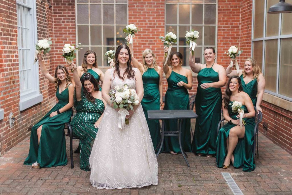 A group of bridesmaids in emerald dresses posing for a wedding portrait at Savage Mill.