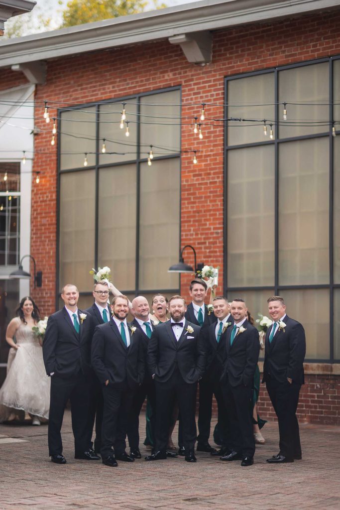 A group of groomsmen posing in front of a brick building at a wedding.