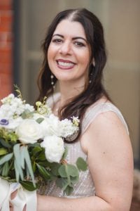 A bride holding a bouquet in front of the Savage Mill, a brick building.