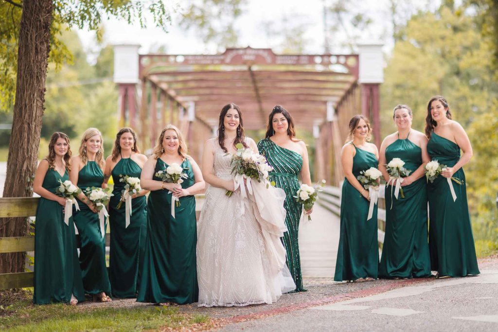 Bridesmaids in emerald dresses standing on a bridge at Savage Mill, posing for wedding portraits.