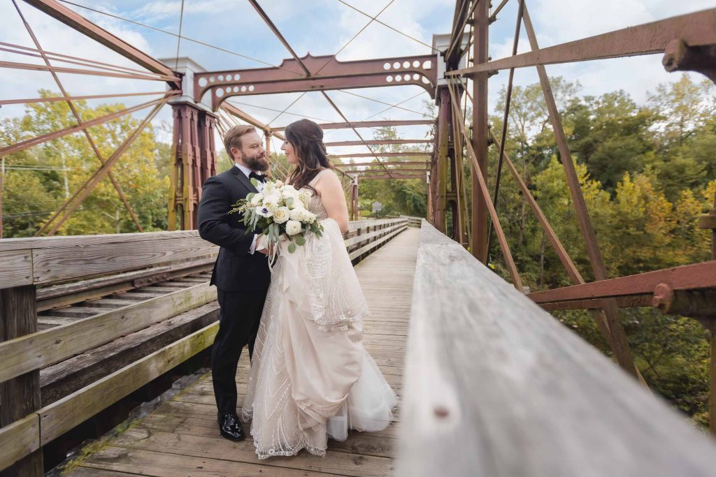 A wedding portrait of a bride and groom standing on the Savage Mill bridge in the fall.