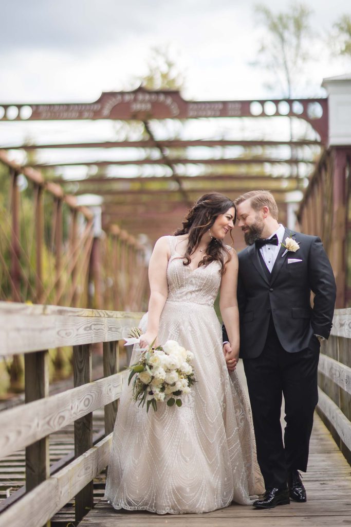 A wedding portrait of a bride and groom standing on a wooden bridge at Savage Mill.