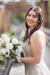 A wedding portrait of a bride smiling while holding her bouquet on a bridge at Savage Mill.