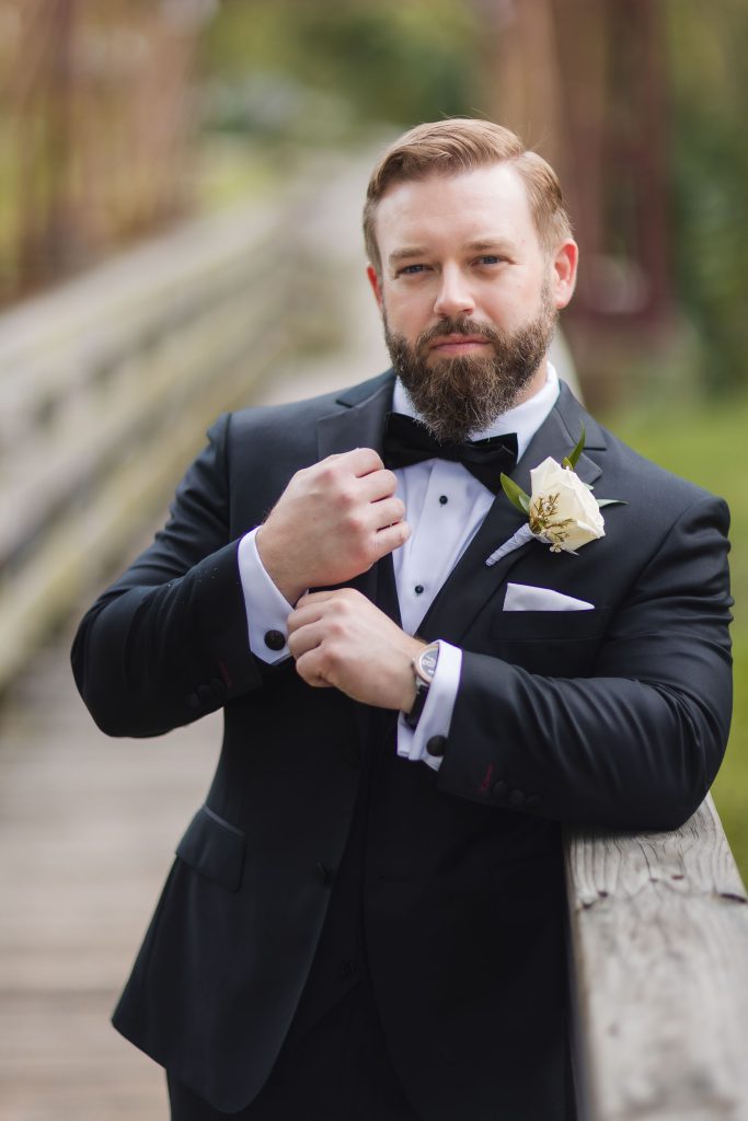 A groom in a tuxedo posing on a bridge at Savage Mill for his wedding portrait.
