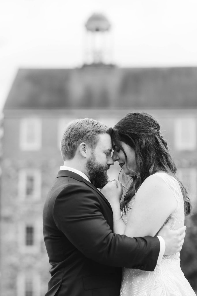 A wedding portrait of a bride and groom embracing in front of the historic Savage Mill building.