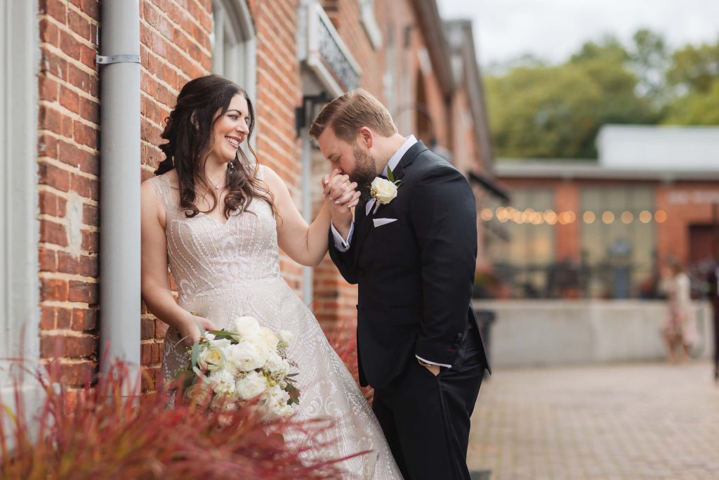 A wedding couple sharing a loving kiss in front of the rustic brick walls of Savage Mill.