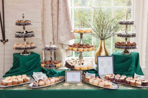 A table full of cupcakes and desserts on a green tablecloth at a wedding in Savage Mill.