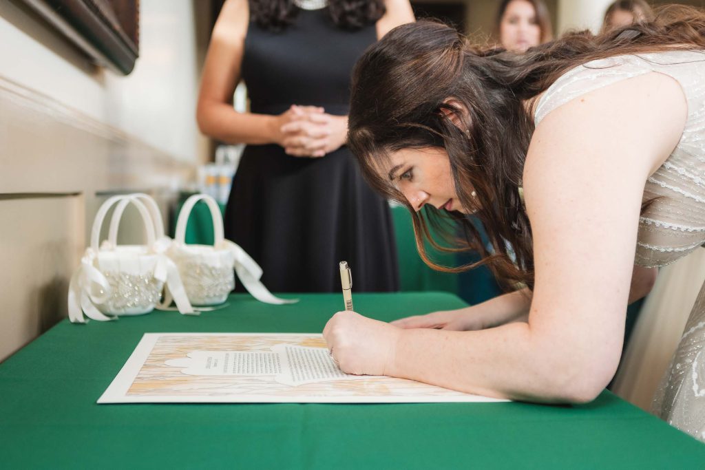 A candid bride signing her wedding vows on a green table at Savage Mill.