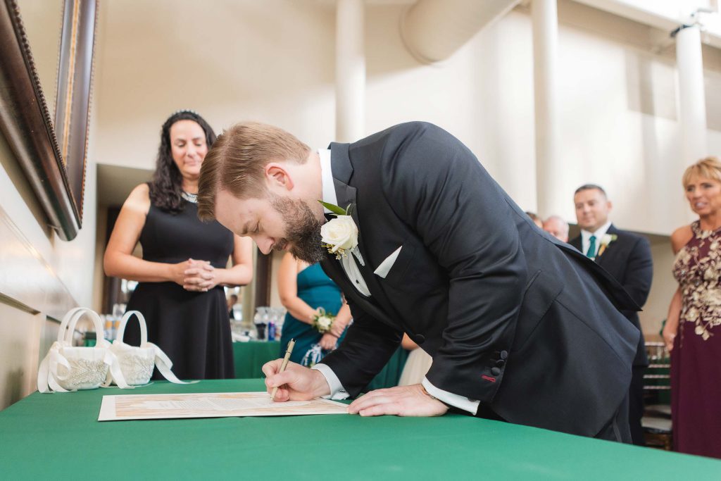 A man signing a wedding certificate in front of a group of people at Savage Mill.