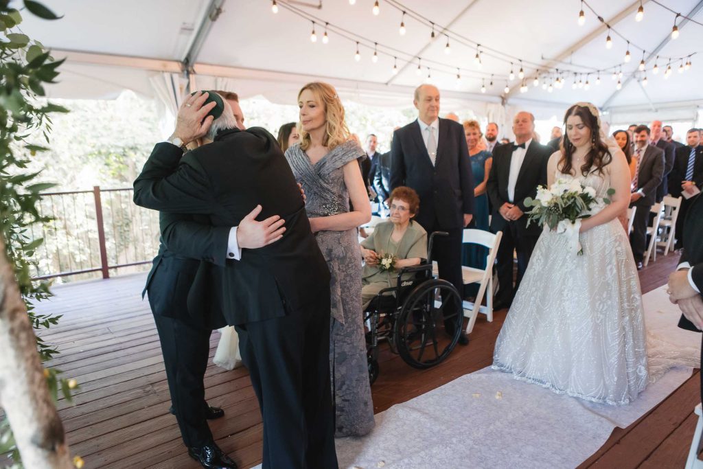 A man affectionately kisses his father during a wedding ceremony at Savage Mill.
