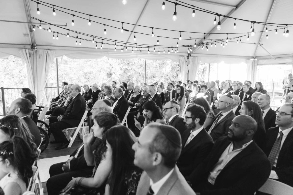 A group of people sitting in a tent watching a wedding ceremony at Savage Mill.