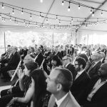 A group of people sitting in a tent watching a wedding ceremony at Savage Mill.
