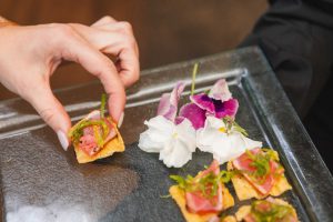 A person holding a tray of appetizers with flowers on it at a wedding in Savage Mill.