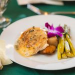 A white plate with food and a glass of wine at a wedding.