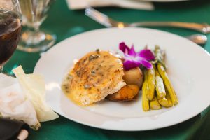 A white plate with food and a glass of wine at a wedding.