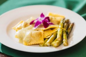 A white plate with asparagus and ravioli on it at a wedding.