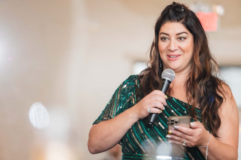 A woman in a green dress speaking into a microphone at a wedding reception.