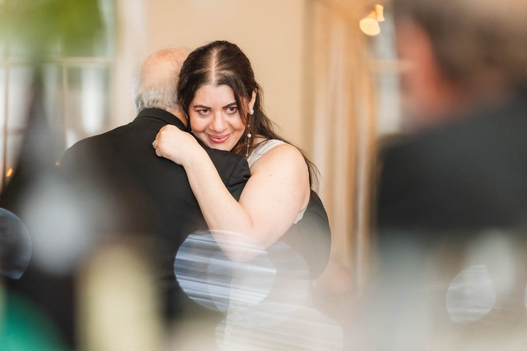 A woman is hugging an older man at a Savage Mill wedding reception.