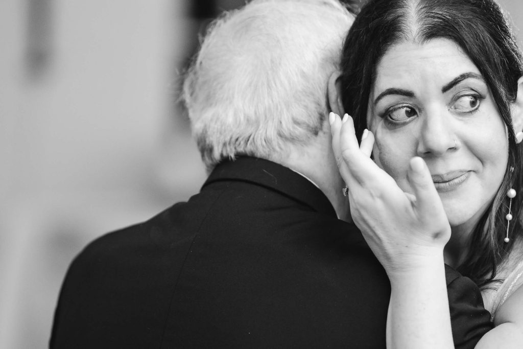 A black and white photo of a woman hugging an older man at a wedding reception.