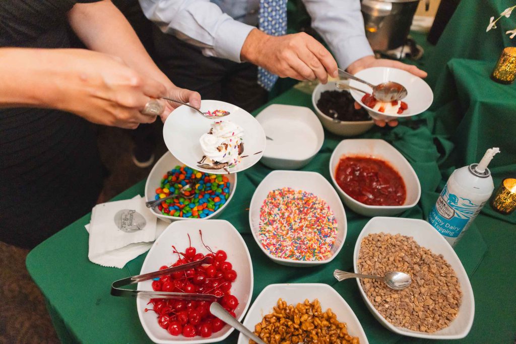 At a table in Savage Mill, a group of people enjoys bowls of candy and ice cream, savoring every delightful detail.
