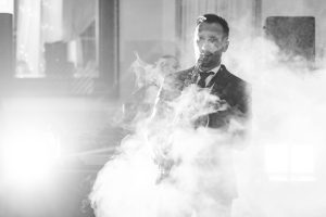 A man in a suit smokes in front of a light at a wedding reception.