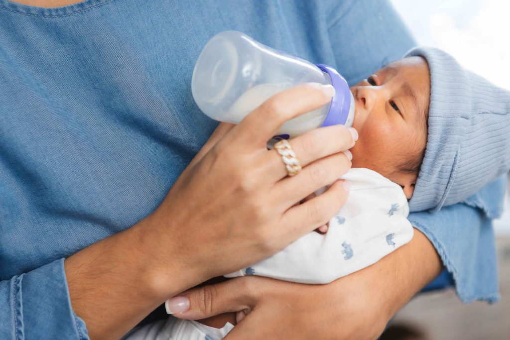 In a family home, a woman tenderly feeds a newborn baby from a bottle.