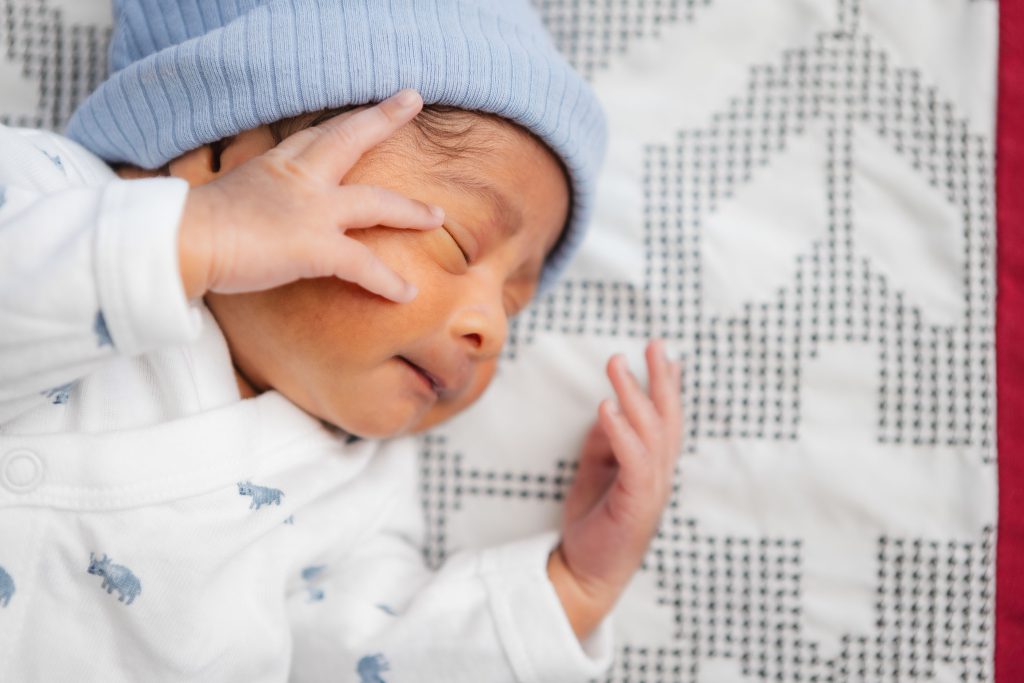 A newborn wearing a blue hat is peacefully laying on a blanket.