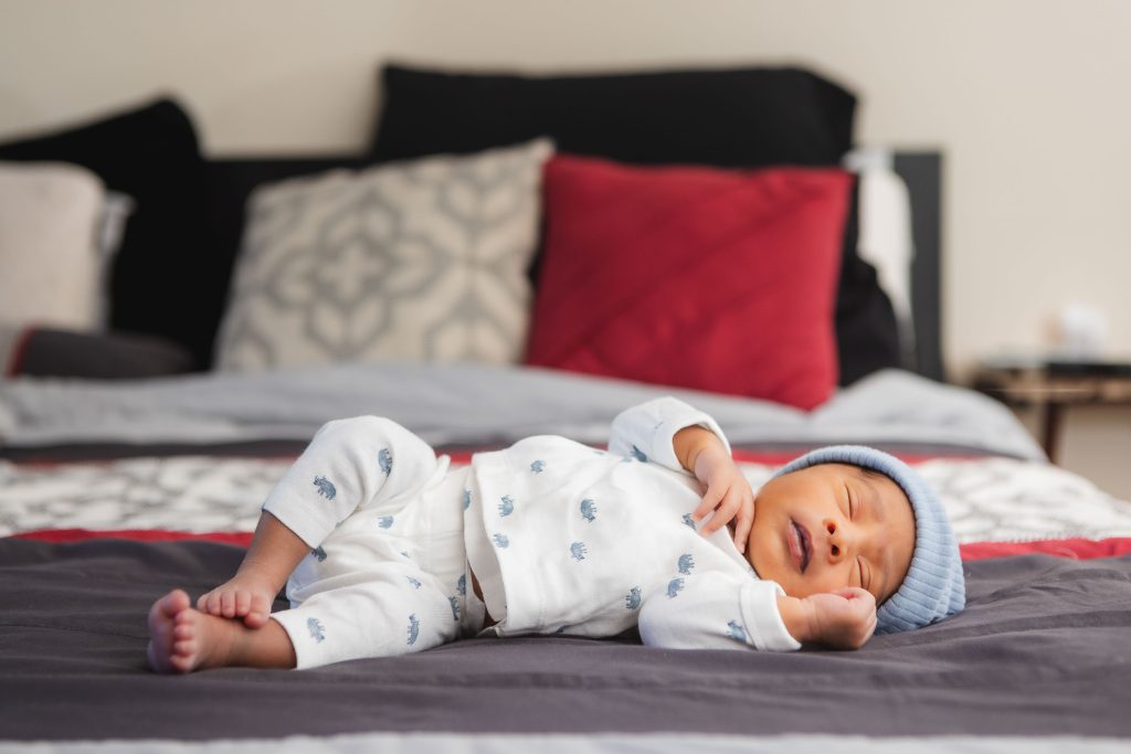 A newborn baby boy is peacefully laying on a bed in a family home.