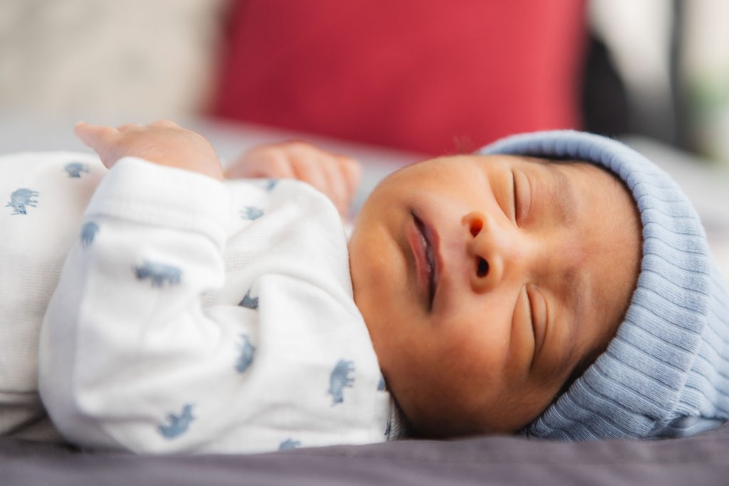 A newborn baby is peacefully laying on a bed wearing a blue hat, while surrounded by the warm ambiance of their family home.