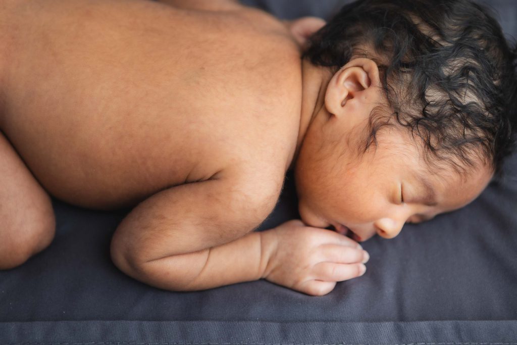 A blissful newborn sleeping on a blue blanket in their family home.