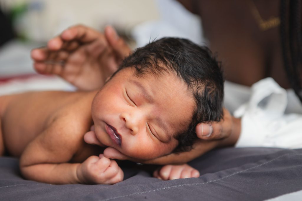 A woman is holding a newborn baby in her arms, capturing a heartwarming family portrait in the comfort of their home.