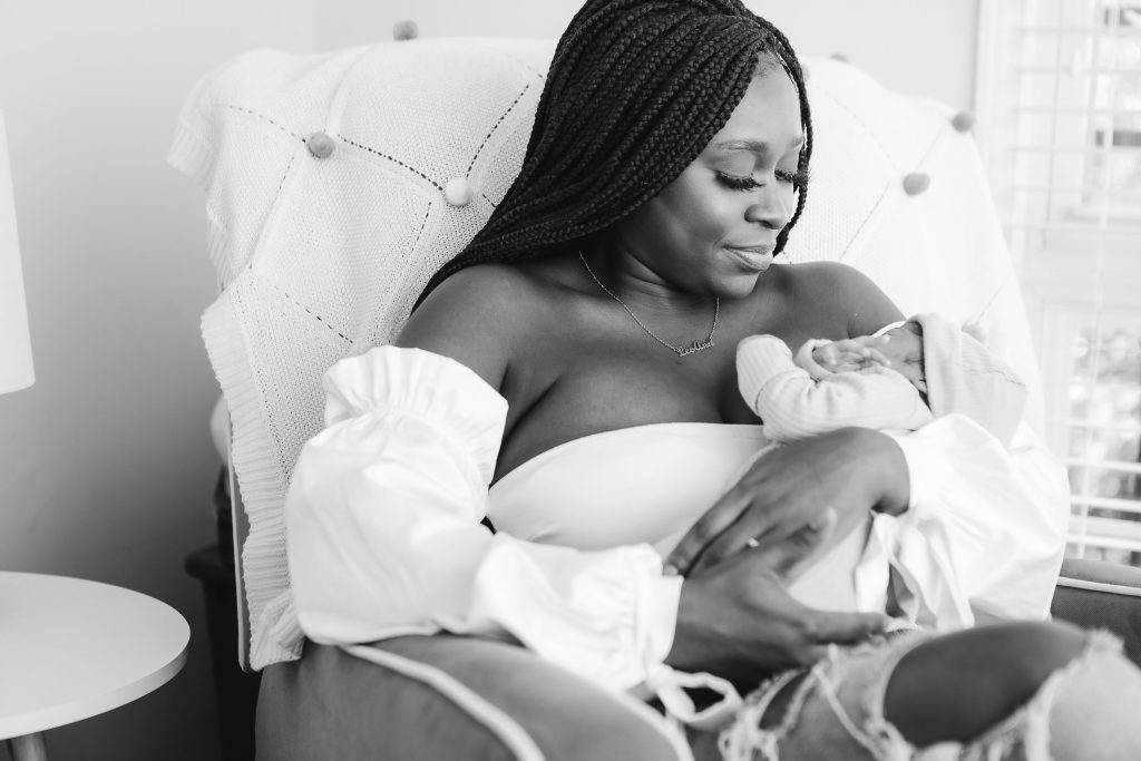 Black and white portrait of a woman delicately cradling her newborn baby in a chair.