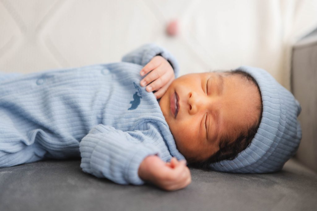 A newborn sleeping in a blue outfit, capturing precious portraits in their family home.