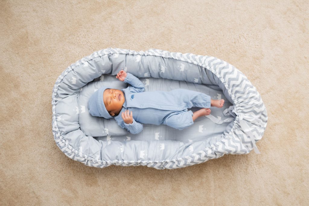 A newborn baby boy is peacefully laying in a blue baby bed, capturing precious family home moments through endearing portraits.